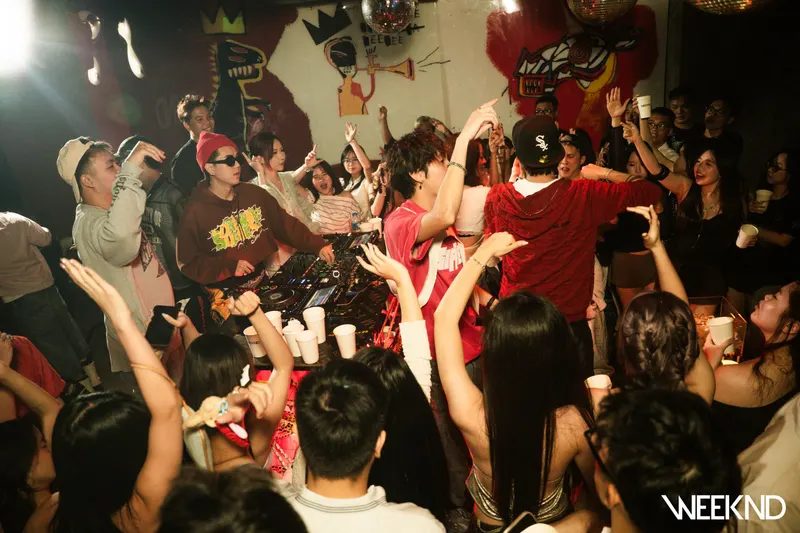 DJ booth trước bức tường graffiti nhiều màu, khách nhảy sát bục